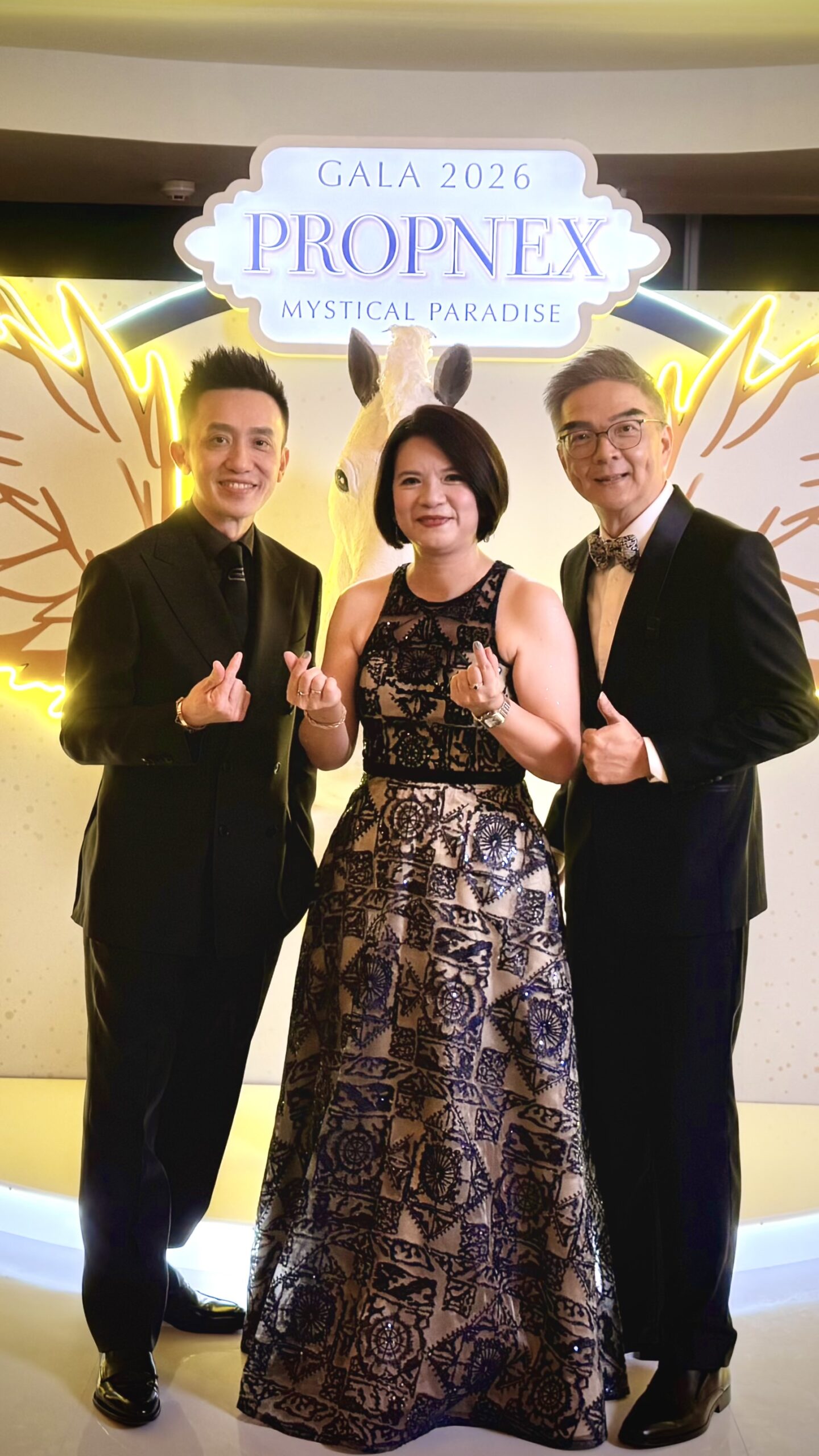 Three attendees posing at the PropNex Gala 2026 Mystical Paradise backdrop.