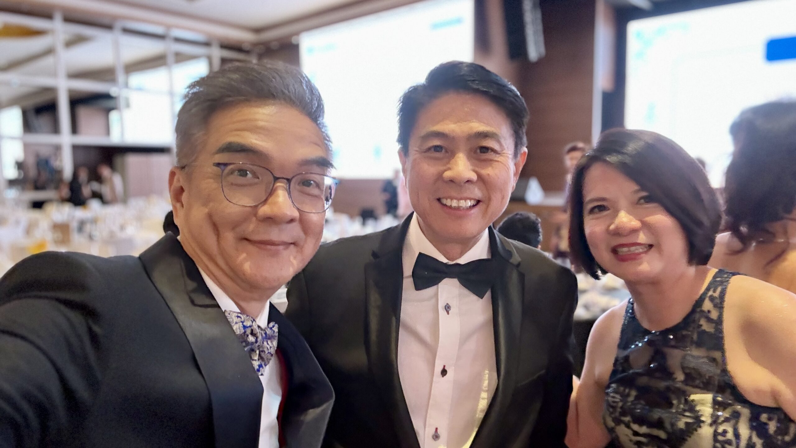 Three attendees dressed in formal evening wear posing together in the ballroom.